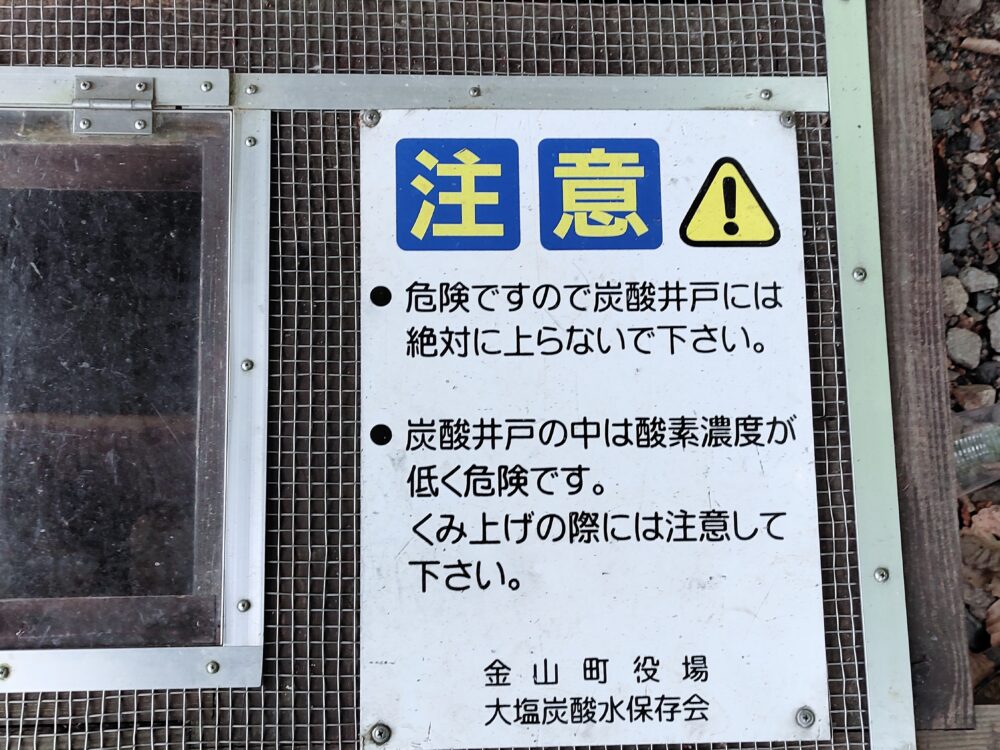 塞がれた井戸の上に掲示されている金山町役場および大塩炭酸水保存会による炭酸井戸に上らないよう呼びかける注意書きの画像