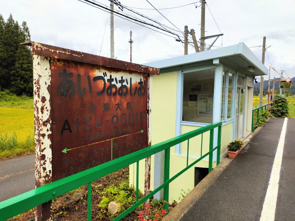 JR只見線会津大塩駅にある、赤く錆びた「あいづおおしお」の看板と無人の駅舎の画像