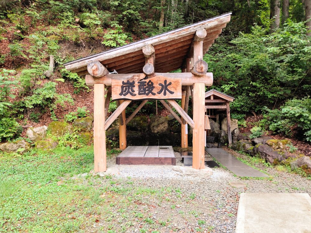 大塩天然炭酸場にある塞がれた井戸と「炭酸水」の看板が掲げられた斜めに傾けた屋根がある木造の東屋の画像